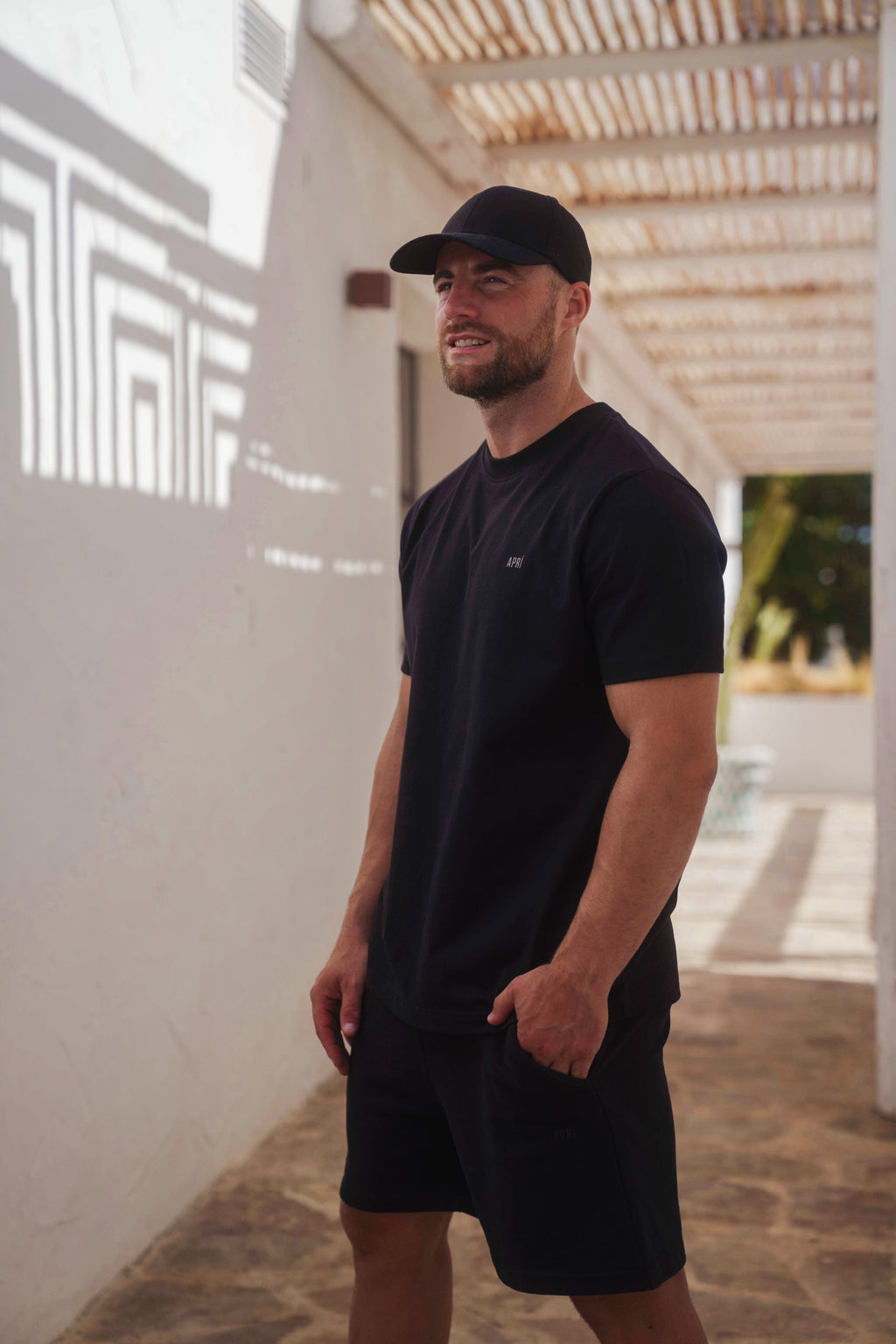 Man wearing a black t-shirt and shorts standing outdoors.