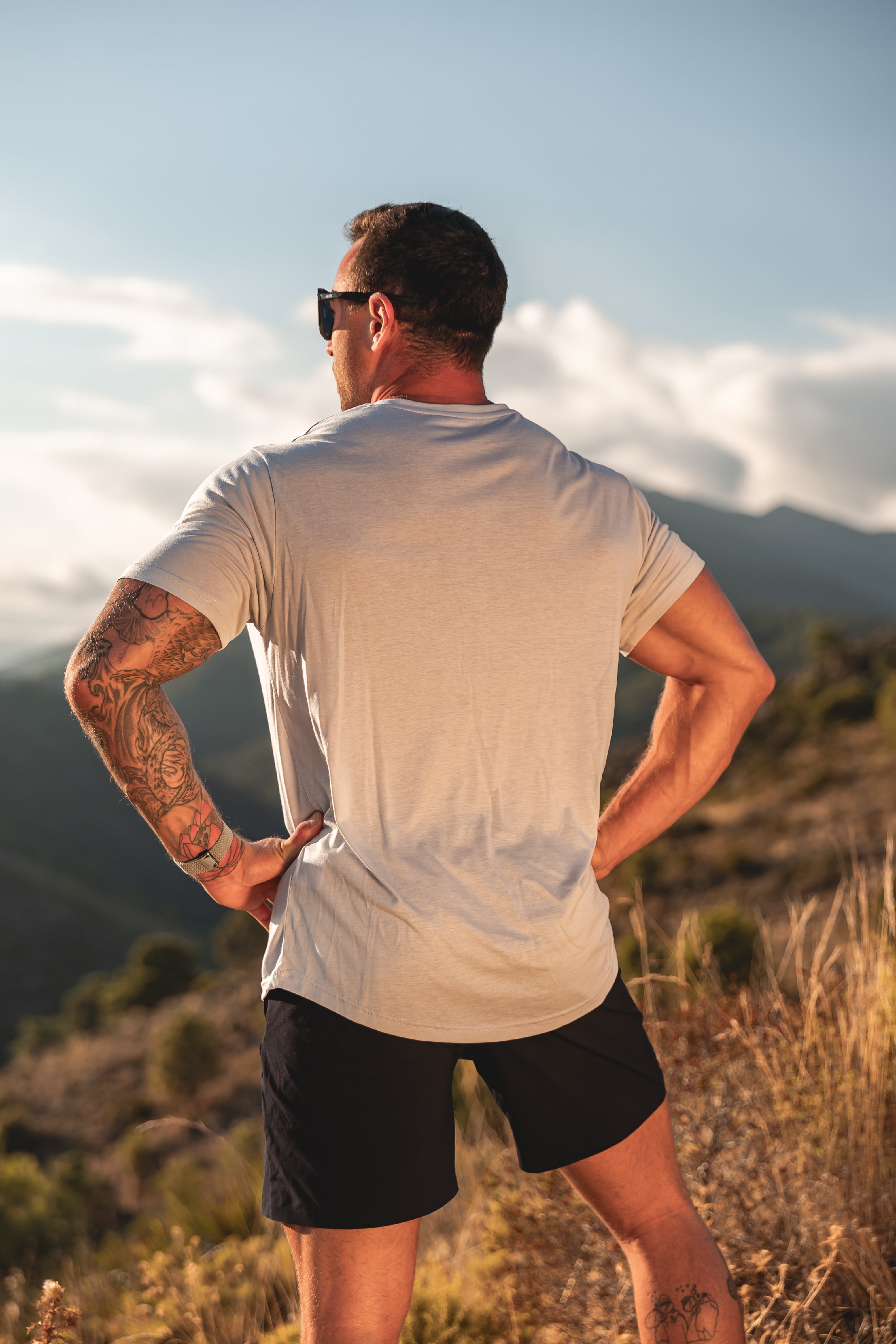 Man standing in a field with mountains in the background. Luna rock grey lyocell t-shirt running.